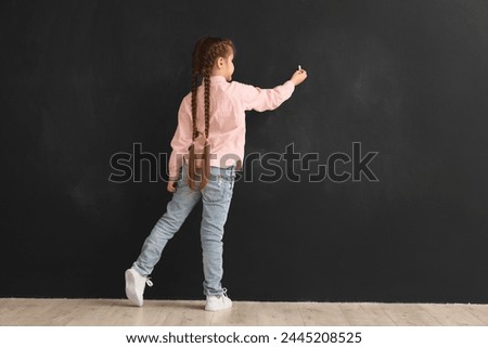 Little girl drawing with chalk piece on blackboard, back view. Children's Day celebration