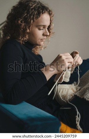 A young woman dressed in a black sweater knitting using knitting needles. Enjoying cozy hobby.