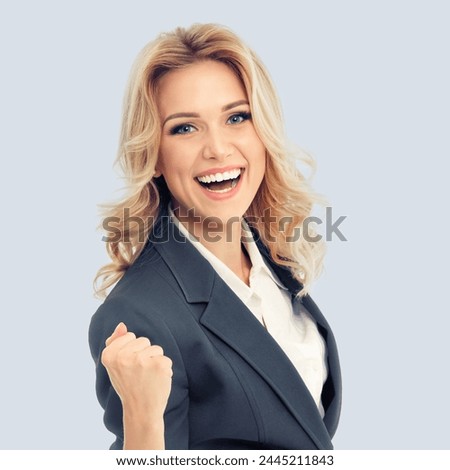Happy gesturing businesswoman in grey confident suit, isolated over against gray background. Caucasian blond model in business success concept. Square composition image. Royalty-Free Stock Photo #2445211843