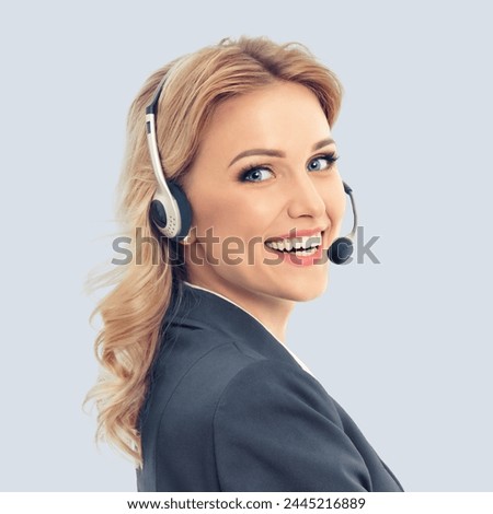 Call center. Smiling female support phone operator in headset, in grey confident suit, isolated over against gray background. Customer service help consulting. Square composition image. Royalty-Free Stock Photo #2445216889