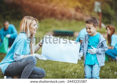 Finished collecting garbage in nature, mother and son are smiling with happiness and pride. They are in focus as they hold the sign in their hands and show it to the camera