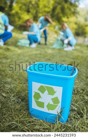 Recycling bin in focus. In the field. With a sign on it. In the background, volunteers are cleaning up the garbage park. Royalty-Free Stock Photo #2445231593