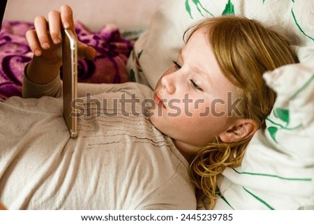 Little girl lying in bed with a mobile phone in her hand.