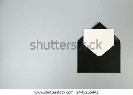 Top view of black envelope, white card on grey background. Post flat lay. Copy space.