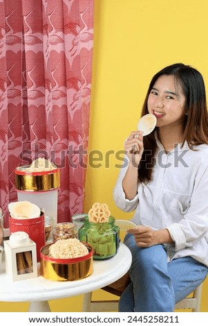 Indonesian Young Girl Enjoy Eating Traditional Snack Popular for Eid Al Fitr, Rengginang, Emping, Simping, Peanuts, Kembang Goyang  Royalty-Free Stock Photo #2445258211