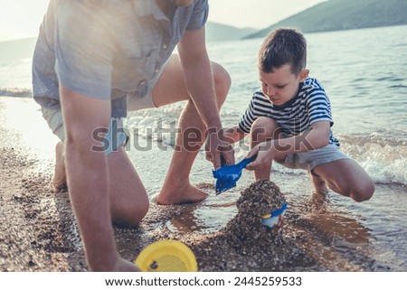 Photo of a little boy playing in the sand with his father, fully equipped with a beach supplies.