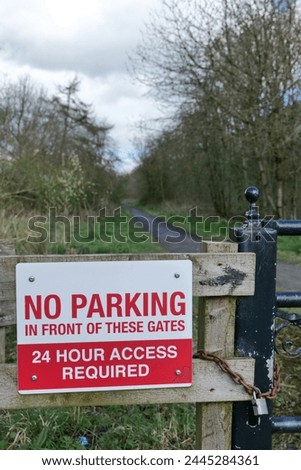No parking sign attached to fence beside padlocked gate, in red and white. Sign says access is required 24 hours a day.