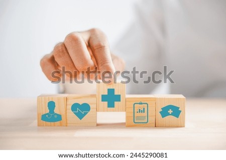 Captured in an image, Hand clutches wooden block featuring healthcare and medical icons. Reflects safety, health, and family well-being, symbolizing pharmacy and heart care. health care concept