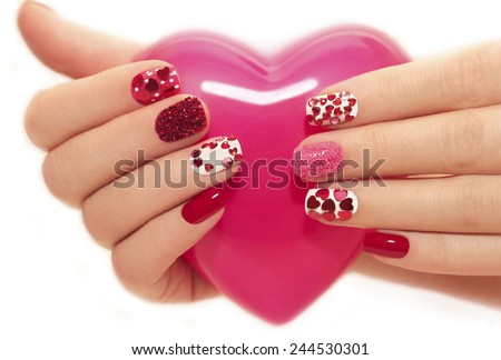 Manicure with rhinestones in the shape of hearts and pink balls on white and red nail Polish on a white background. Royalty-Free Stock Photo #244530301