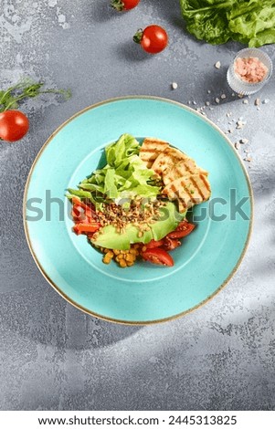 Top view of a grilled chicken and avocado salad bowl with vegetables, served on a textured surface. Royalty-Free Stock Photo #2445313825