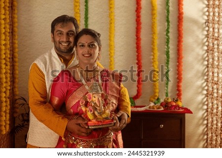 Portrait of happy young couple holding an idol of Lord Ganesha
