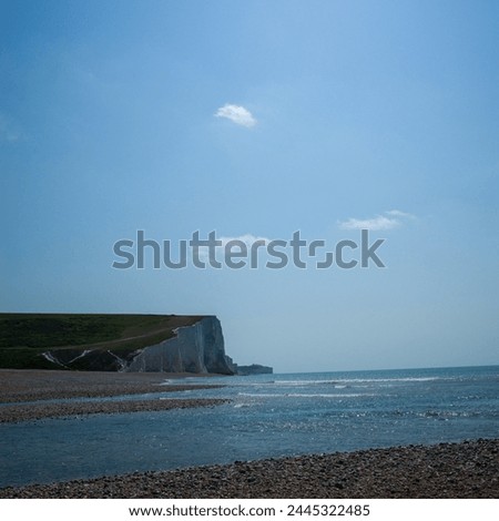 A section of the Seven sisters white cliff from the right under a blue sky. The lower part of the picture is the sea and pebble beach 
