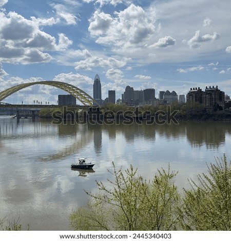 Boat on the river in front of a city skyline and a bridge at midday with a cloudy blue sky.