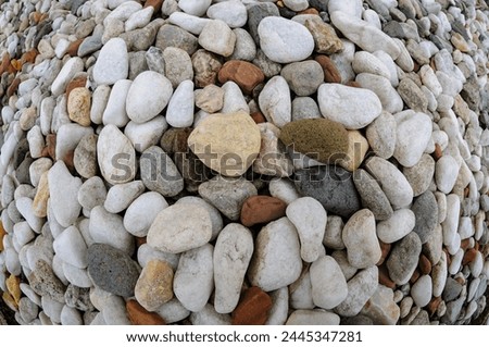 An assortment of rounded pebbles in various colors forms a spiral design on sandy ground.