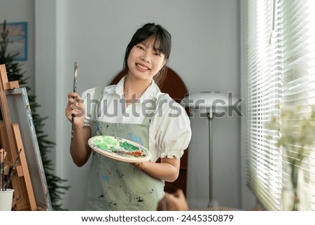 A young artistic girl holds a paintbrush and a paint tray and looks cheerfully at the camera.