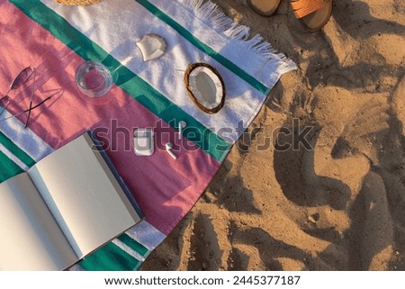Wireless headphones, notepad, glass of water, coconut and sunglasses on the striped towel on the sand. Summer vacation lifestyle concept