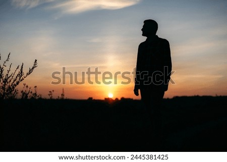 The silhouette of a man against the background of a beautiful sky with clouds. Blue sky, yellow orange sun, sunset. A lonely man walking in nature. Finding yourself, thought