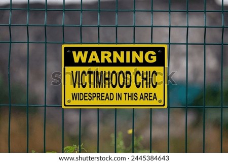 Warning sign on a fence stating in "Warning, victimhood chic widespread in this area".
