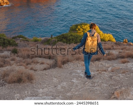 Young woman hiking on rocky beach in Spain, Benidorm. Watching the choppy sea and the bay. traveler enjoying freedom in serene nature landscape Royalty-Free Stock Photo #2445398651