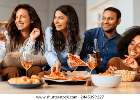 Multiracial friends gather around a living space with slices of pizza and wine, sharing food and conversations in a cozy atmosphere