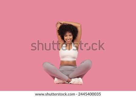 A happy african american woman in a yoga pose with hands clasped above her head against a pink background Royalty-Free Stock Photo #2445400035