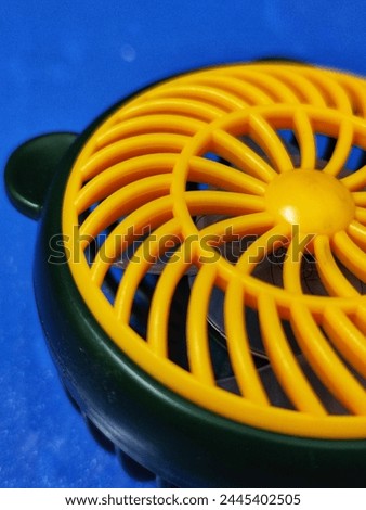 picture of part of a small portable electronic fan in yellow and black with a blue background