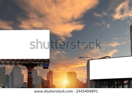 Two large billboards are in the foreground of a city skyline. The sky is cloudy and the sun is setting, creating a moody atmosphere