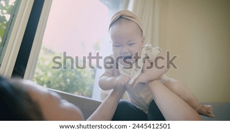 Happy Mother and baby playing bonding activity together in living room. little cute Asian baby infant child girl excited laughing and fun spend quality time on sofa Family having fun at home