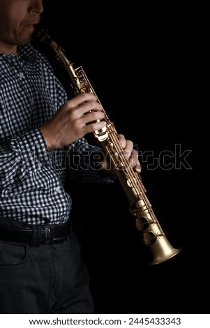 soprano saxophone in hands on a black background Royalty-Free Stock Photo #2445433343