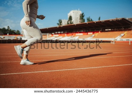 Cropped picture of an unrecognizable young female track athlete running on running track on stadium. Legs running on stadium. Cardio exercise and workout. Sportswoman jogging on stadium running track.