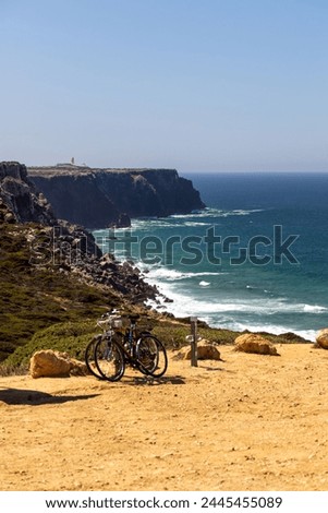 Bicycle parking with bikes on a surfing beach in Portugal - in the background cliff with a lighthouse and an ocean with foamy waves