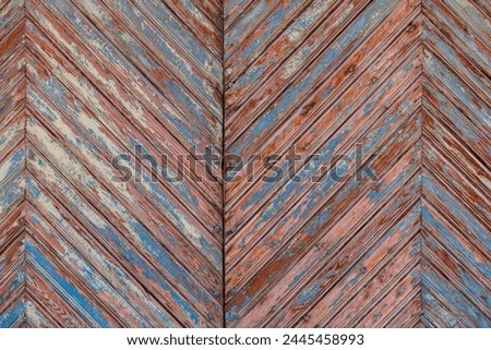 Artistic old wooden planks gate chevron pattern with peeled brown and blue paint layers under sun-bleached blue paint layer. Full-frame flat background and texture.