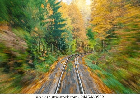 The photo taken fron a Canadian national railway train in motion.  Slow shutter speed to show motion.  Railroad tracks winding through autumn color forests