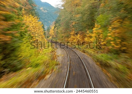 The photo taken fron a Canadian national railway train in motion.  Slow shutter speed to show motion.  Railroad tracks winding through autumn color forests