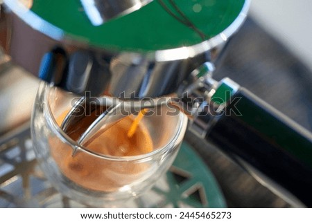 A dynamic Dutch angle captures the precise moment coffee is poured into a glass cup from a modern, green and silver espresso machine Royalty-Free Stock Photo #2445465273