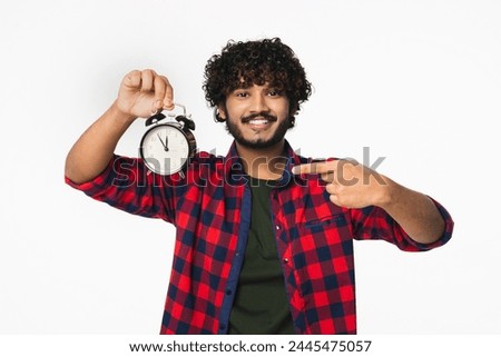 Cheerful young Indian man in casual clothes showing time on clock isolated over white background. Hindi boy having deadline, checking on time, hurrying up