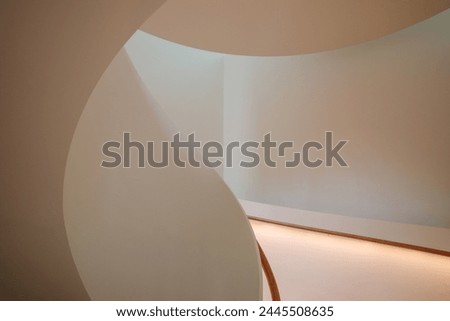 Interior staircase featuring a smooth curve, with warm light emanating from the built-in illumination along the handrail.  Royalty-Free Stock Photo #2445508635