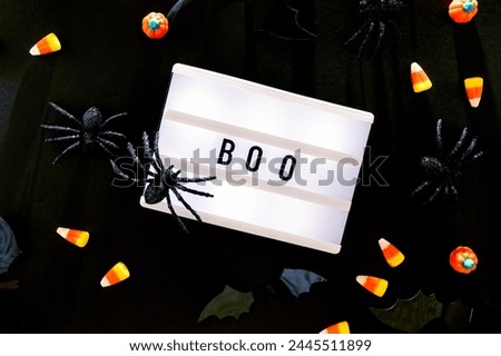 Traditional Halloween decor and candies on black background with word Boo on the lightbox