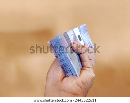 a hand holding a large number of ten thousand rupiah notes