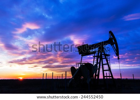 Operating oil and gas well profiled on sunset sky Royalty-Free Stock Photo #244552450
