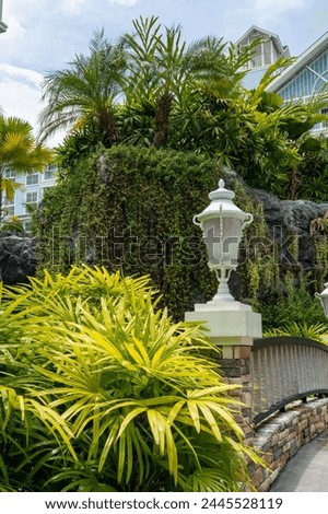 A white decorative lantern sits on the railing of a swimming pool bridge against a backdrop of lush tropical vegetation in a condominium courtyard.