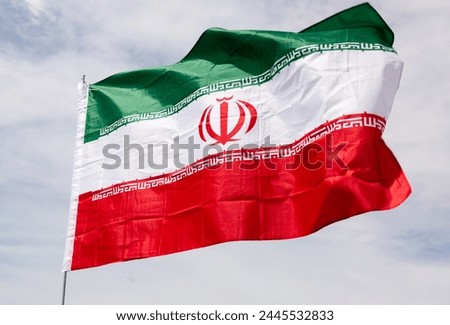 Big flag of Iran fastened on stick against background of blue sky under daylight Royalty-Free Stock Photo #2445532833