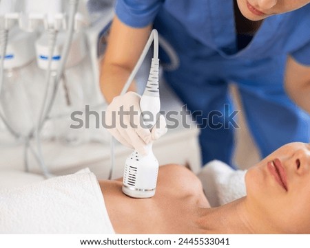Young adult female patient receiving professional hardware procedure on chest and neck area at beauty clinic using cooling attachment to alleviate inflammation, rejuvenate skin and enhance complexion