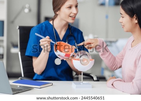 Female Caucasian ophthalmologist explains about eye diseases using the eye model with an Asian female patient At the table in the hospital examination room, Glaucoma, Cataract, Diabetic Retinopathy