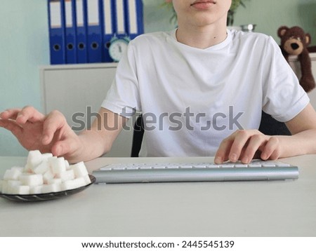 Teenager guy eats sugar while working at the computer at home. Sweet addiction, uncontrolled consumption of sugar in teenagers and children Royalty-Free Stock Photo #2445545139