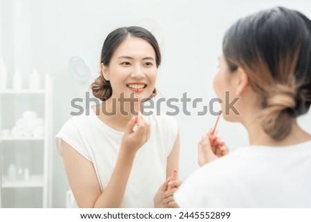 Beautiful Asian woman sit in front of a mirror and smile on makeup. face of a healthy woman applying makeup. Advertisement, lifestyle , cosmetics, makeup accessories, beauty activity, beautician Royalty-Free Stock Photo #2445552899