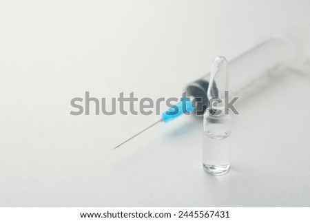 Glass ampoule with liquid and syringe on white background, closeup. Space for text