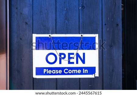Blue and white plastic sign or symbol letter Open Please come Attached to the blue wooden door is background. Attention and alert.