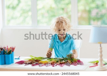 Child creating picture with colorful leaves. Art and crafts for kids. Little boy making collage image with rainbow plant leaf. Biology homework for young school student. Creative autumn home fun.