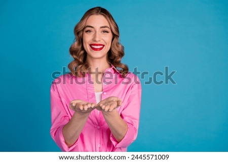 Photo portrait of pretty young girl hold empty space wear trendy pink outfit hairdo isolated on blue color background